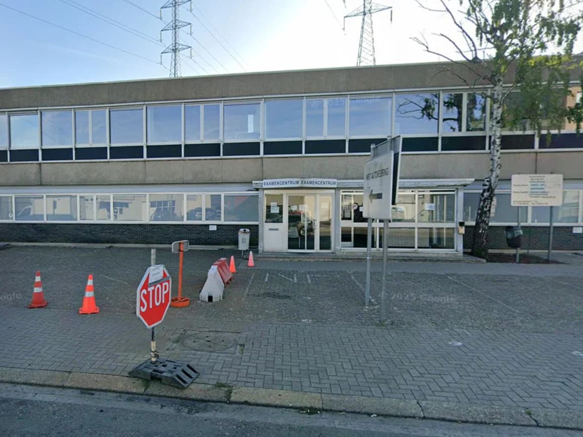 De ingang van het examencentrum in Deurne, een grijs gebouw met twee verdiepingen en de parking ervoor